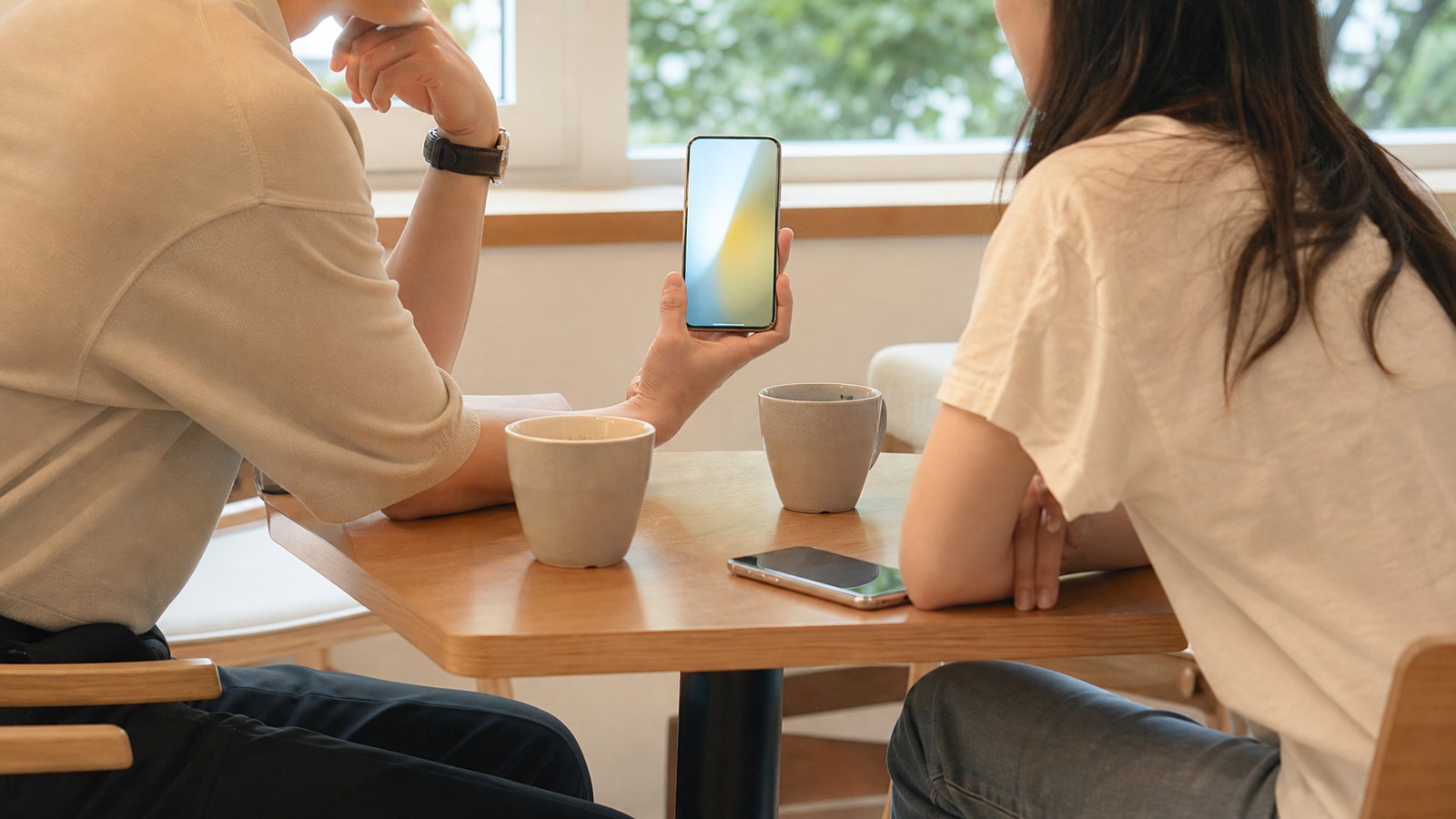 明るいソウルのカフェで、スマートフォンの画面を見せ合う初デートの二人